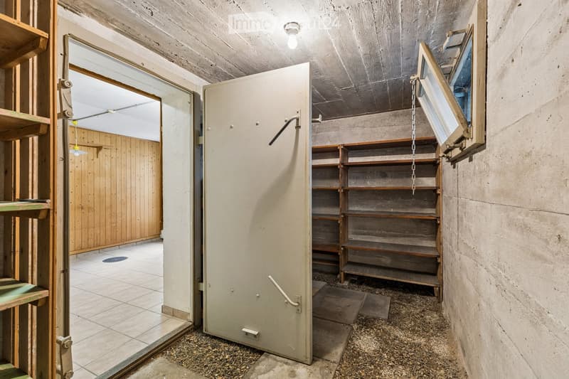 Empty storage area with concrete walls, wooden shelves, and a tiled room visible through an open door.