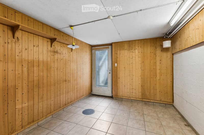 Empty room with wooden panel walls, tiled floor, and a single door with a frosted glass panel. No furniture or equipment is present.