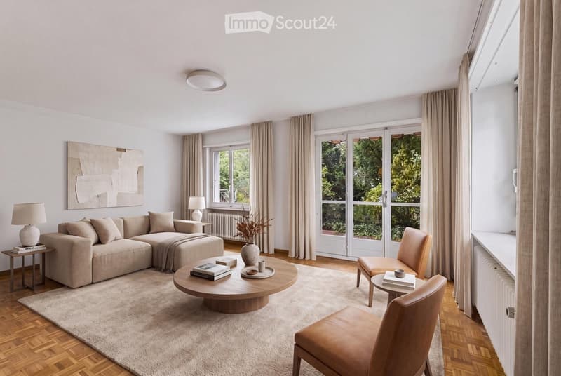 Modern living room with light-colored furniture, large windows, and a view of greenery outside. Features a sectional sofa, coffee table, armchairs, table lamps, and decorative items.