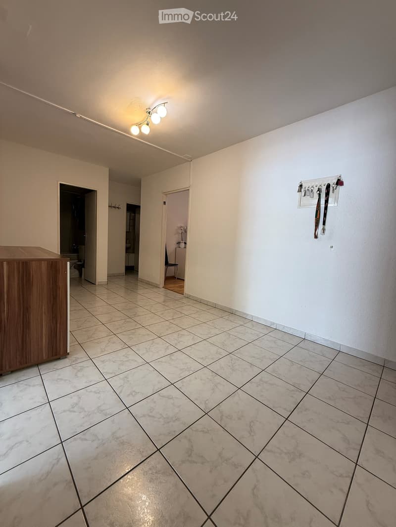 Empty hallway with tiled floor, white walls, and a coat rack with hooks. There are two open doors leading to other rooms.