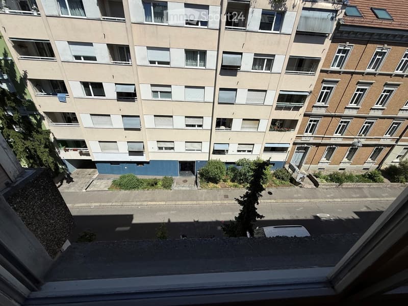 Multi-story residential building with multiple windows, balconies, and a small garden area in front.