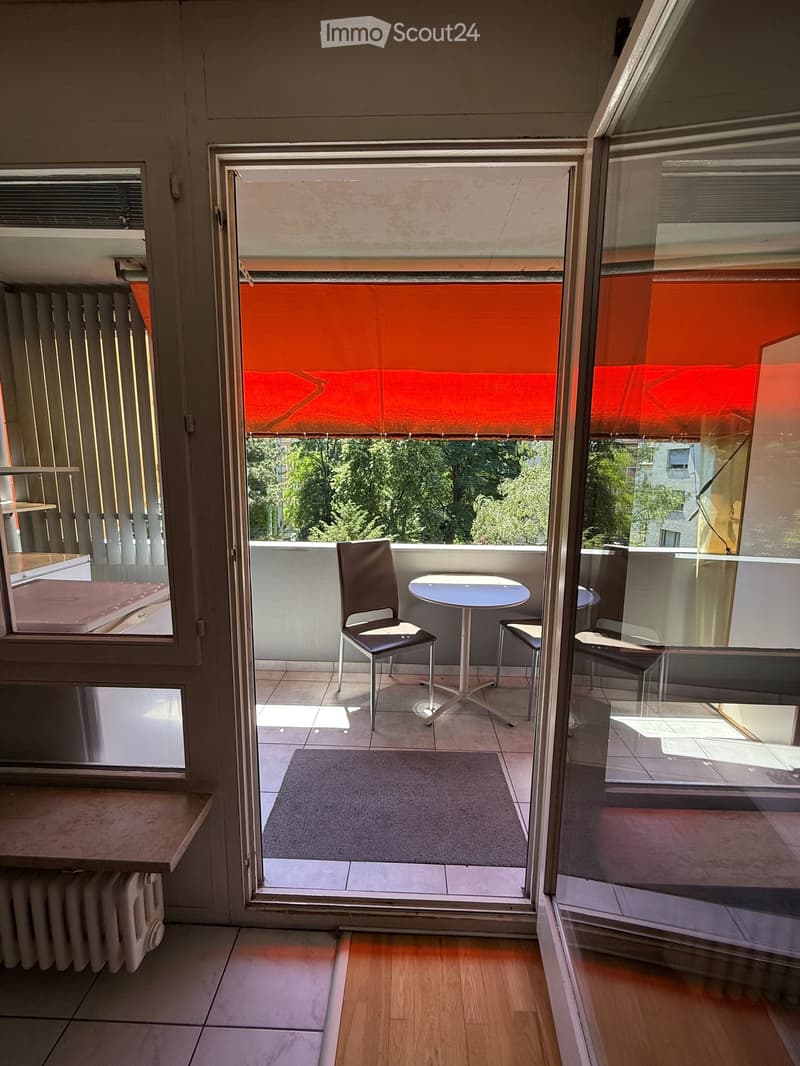 Balcony with a small table and chair, tiled floor, and a view of greenery outside.