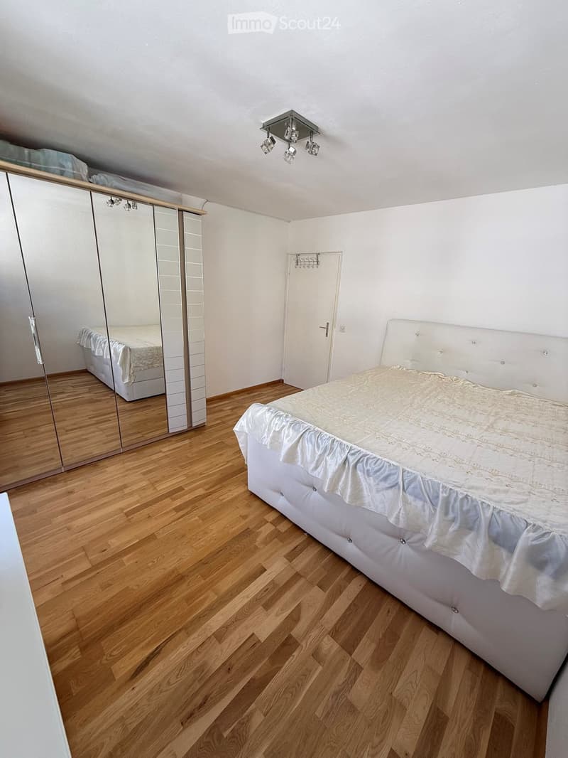 Bedroom with wooden flooring, white walls, a large bed with white bedding, and a mirrored wardrobe.
