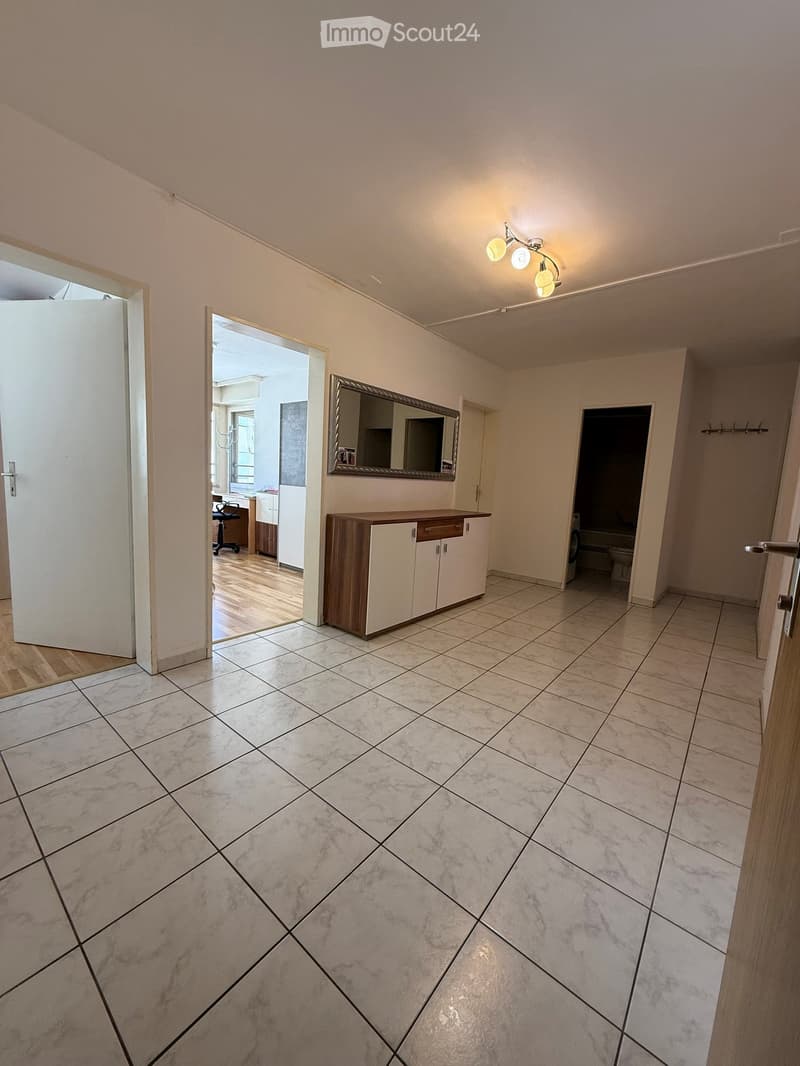 Empty hallway with marble tiled floor, white walls, and several doors leading to other rooms. A small cabinet and mirror are visible in the background.