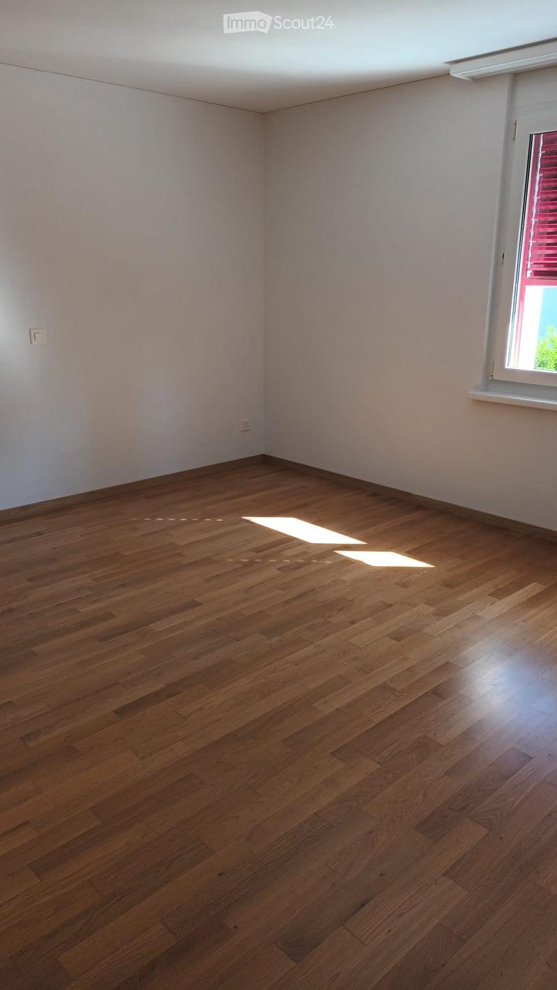 Empty room with wooden flooring and white walls, featuring a single window with blinds and natural light streaming in.