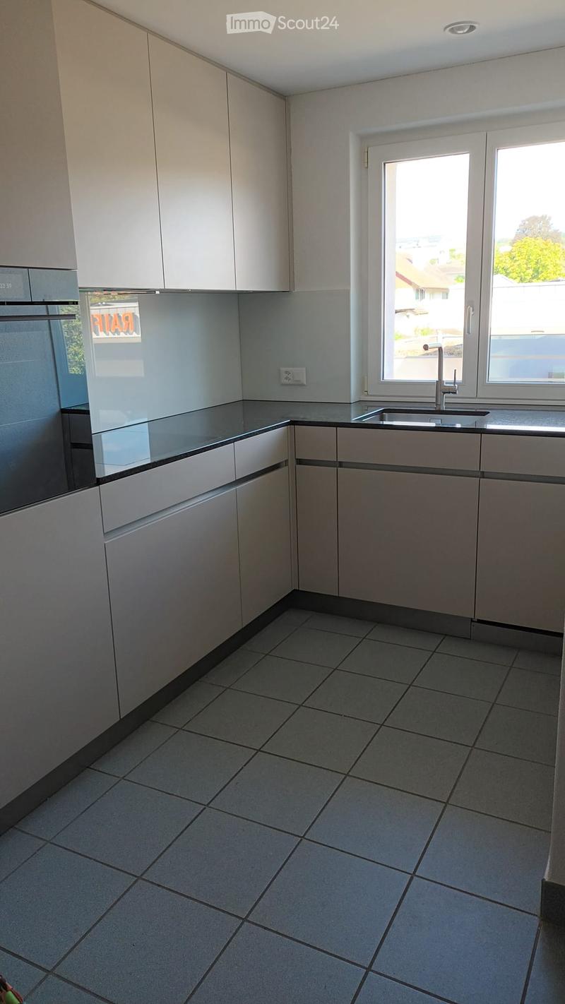 Modern kitchen with light grey cabinets, tiled floor, and a window above the sink.