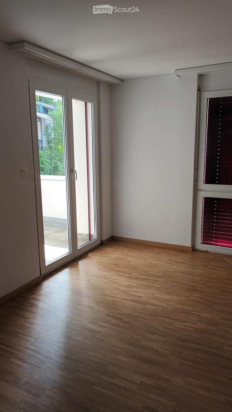 Empty room with wooden flooring, large sliding glass door leading to a balcony, and a window with blinds.