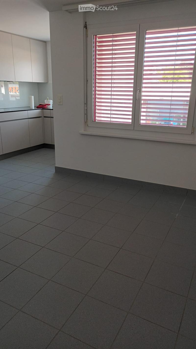 Empty kitchen with tiled floor, white cabinets, and a window with blinds. No furniture or appliances are present.