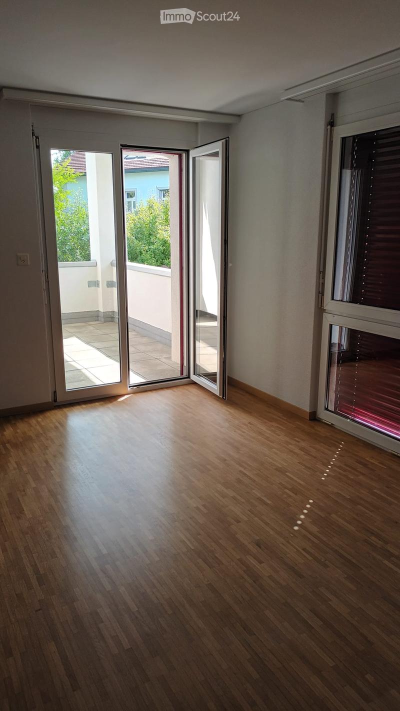Empty room with wooden flooring, large sliding glass doors leading to a balcony, and natural light streaming in.