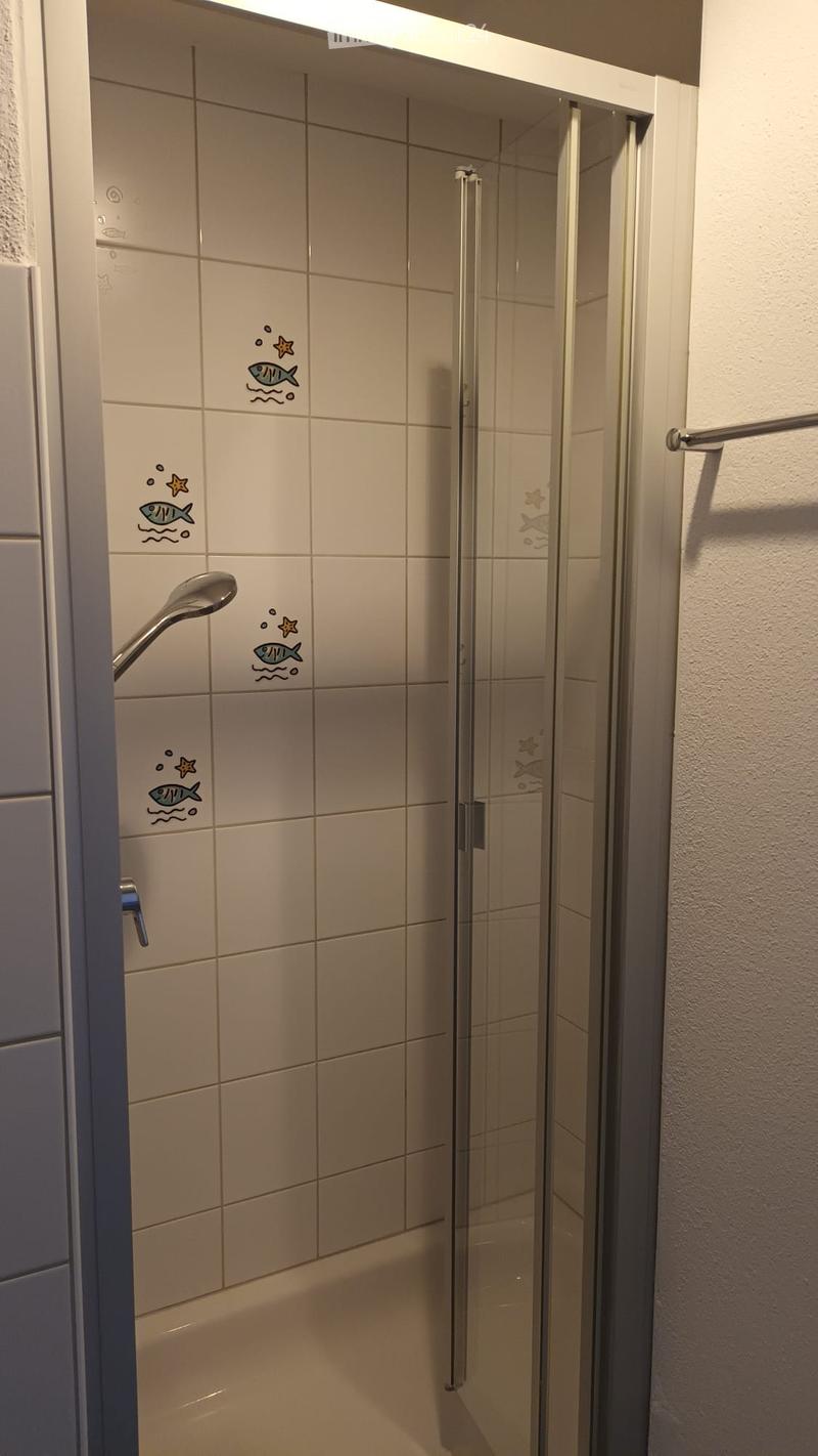 Shower area with beige tiles featuring fish and starfish decals, glass shower enclosure, and a modern showerhead.