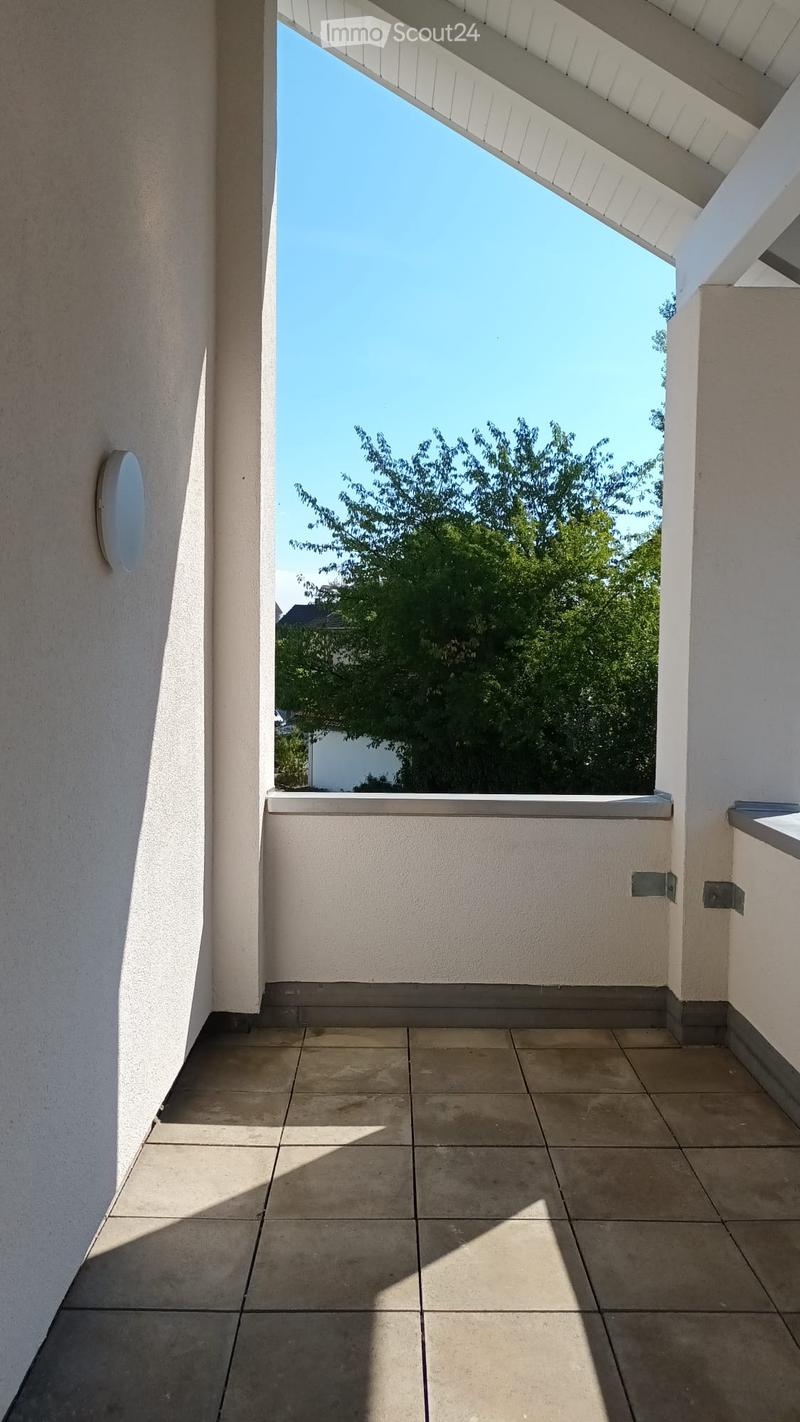Balcony with tiled floor, white walls, and a view of a tree and clear sky.
