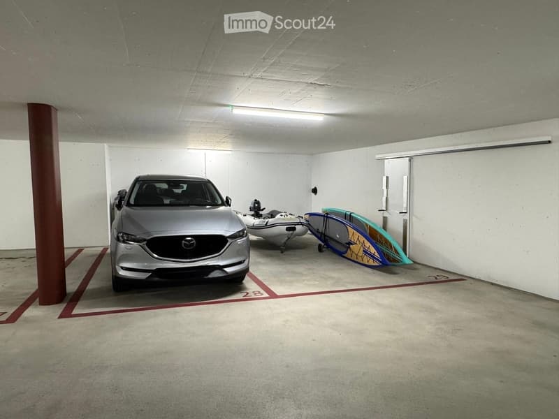Underground parking area with a silver car, a surfboard, and a small watercraft.