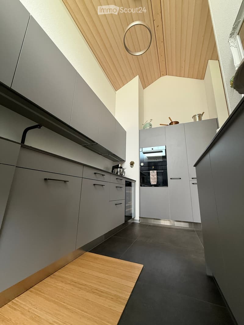 Modern kitchen with grey cabinets, dark tiled floor, and a wooden accent area. Features an oven, kitchen island, and various kitchen appliances.