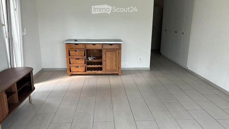 A furnished room with a wooden cabinet, a small table, and tiled flooring.