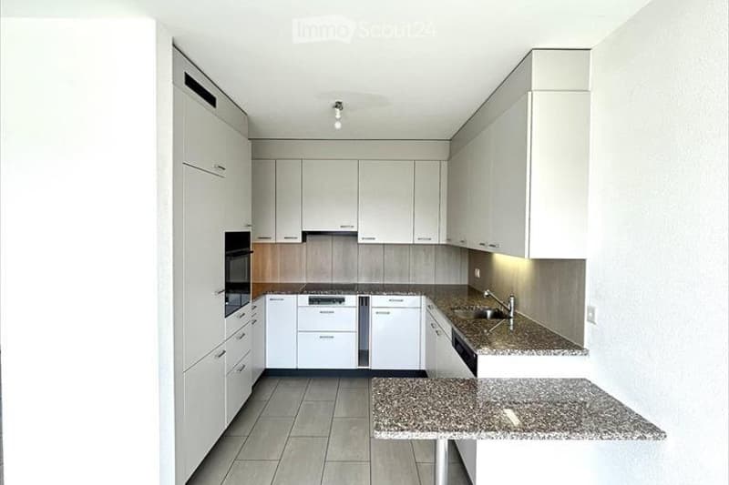 Modern kitchen with white cabinets, granite countertops, and stainless steel appliances including an oven and dishwasher.