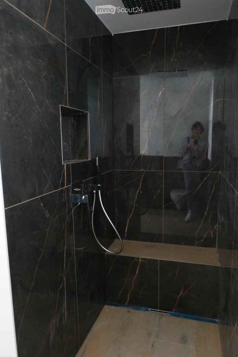 Modern bathroom with black marble walls, glass shower stall, and a built-in shelf.