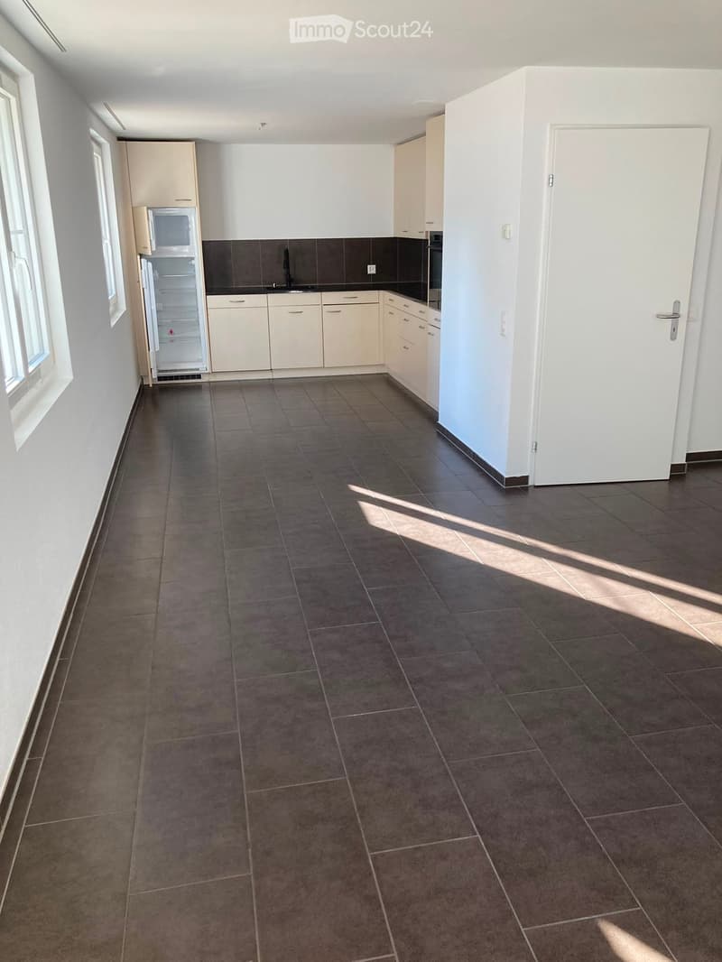 Empty kitchen with tiled floor, white cabinets, and built-in appliances including a refrigerator, microwave, and oven. Sunlight streams in from the left side.
