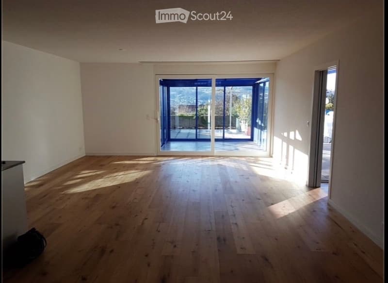 Empty room with wooden flooring, large sliding glass doors leading to a balcony, and white walls.