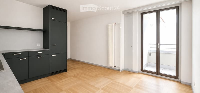 Modern kitchen with dark grey cabinets, light wooden flooring, and a large sliding glass door leading to a balcony.