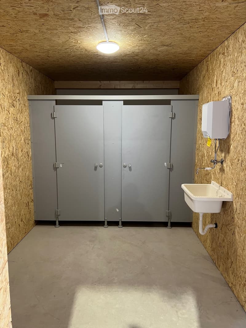 Empty bathroom with wooden walls and ceiling, two stall doors, a sink with a faucet, and a hand dryer on the wall.