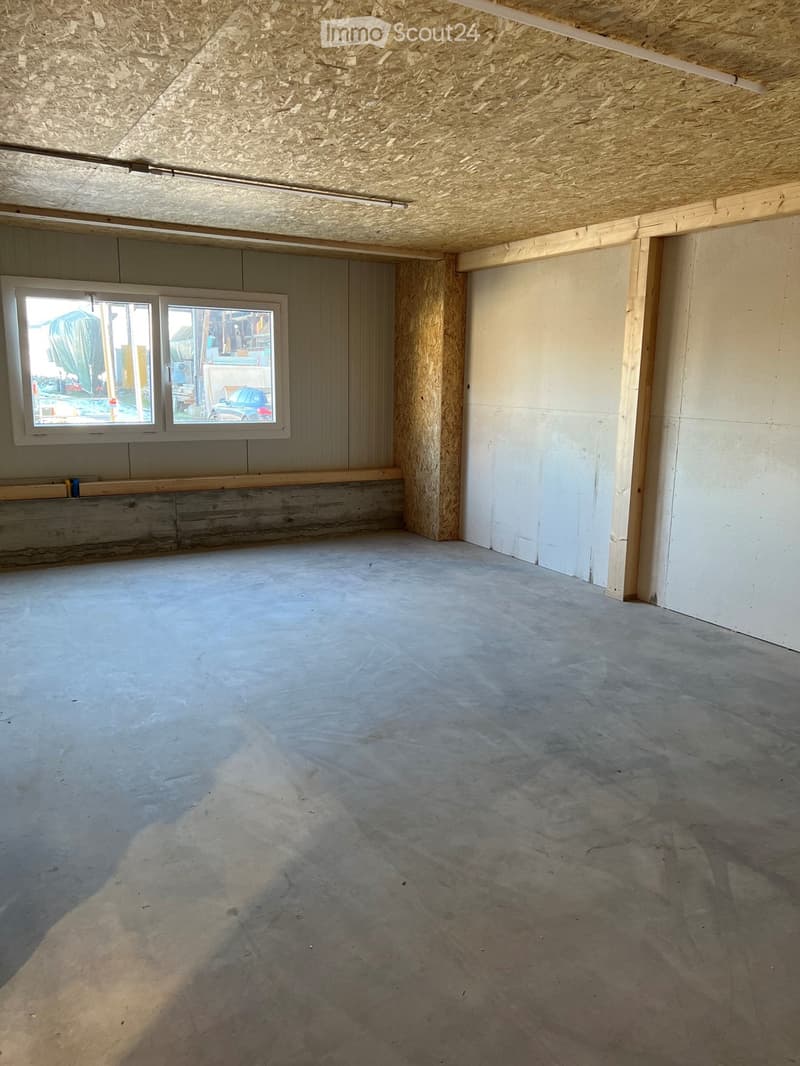 Empty room with concrete floor, exposed wooden beams, and a window with a view of the outside.