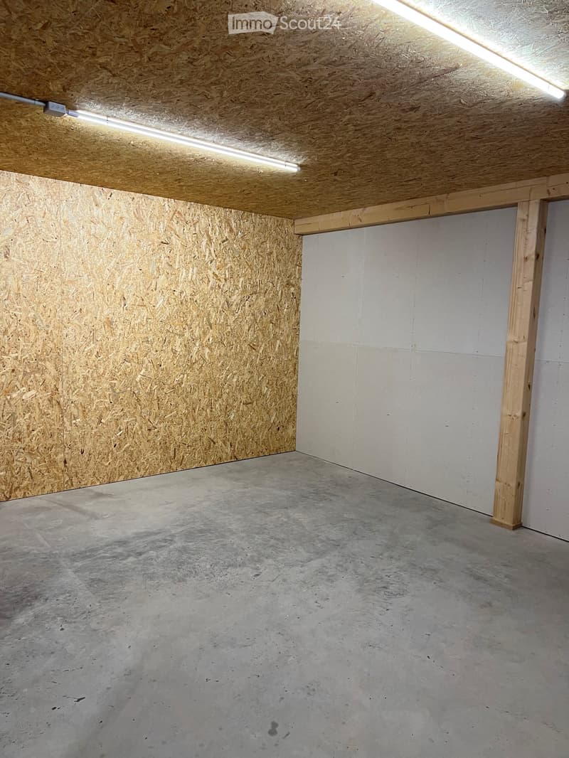 Empty garage with concrete floor, wooden ceiling, and exposed wooden beams. No furniture or equipment present.