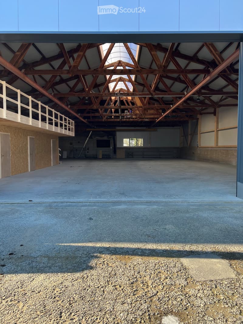 Large industrial-style building with a high, wooden-trussed ceiling and concrete floor, featuring a balcony area and minimal furnishings.