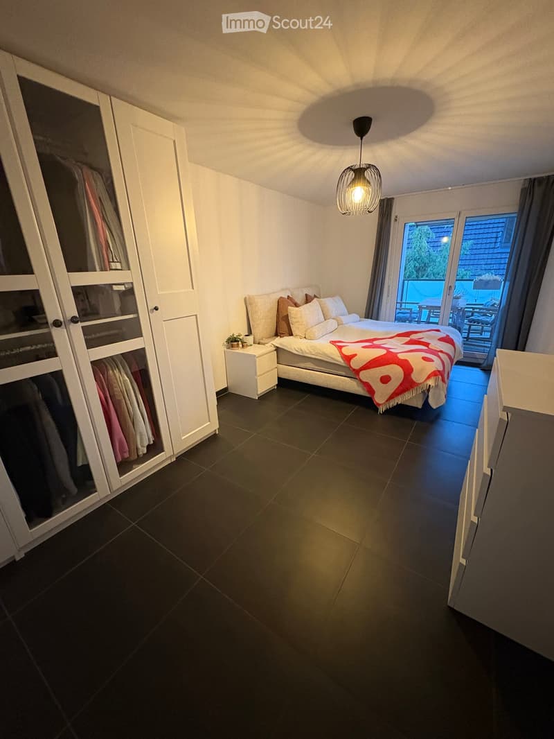 Modern bedroom with a large bed, nightstand, wardrobe, and a view to a balcony or terrace area.