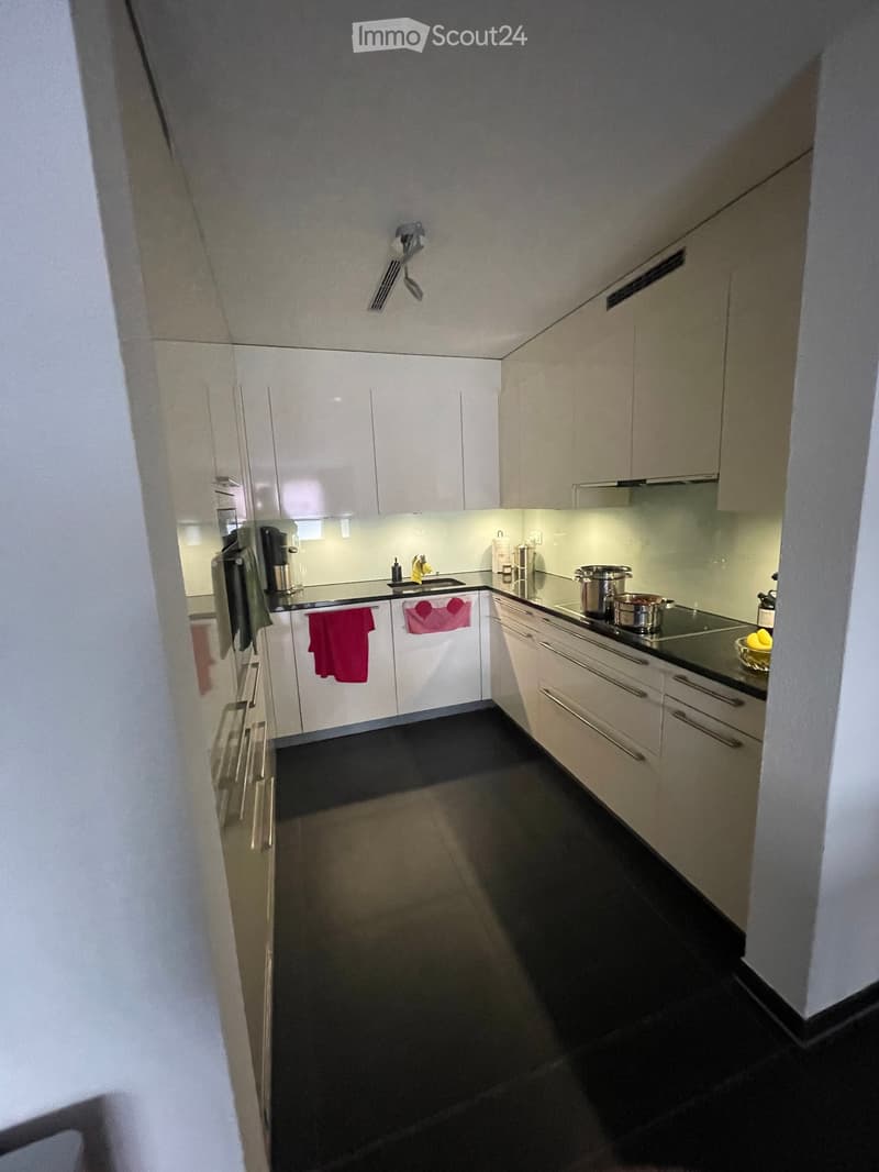 Modern kitchen with white cabinets, stainless steel appliances, and a black countertop. Features include a refrigerator, oven, sink, and various kitchen items.