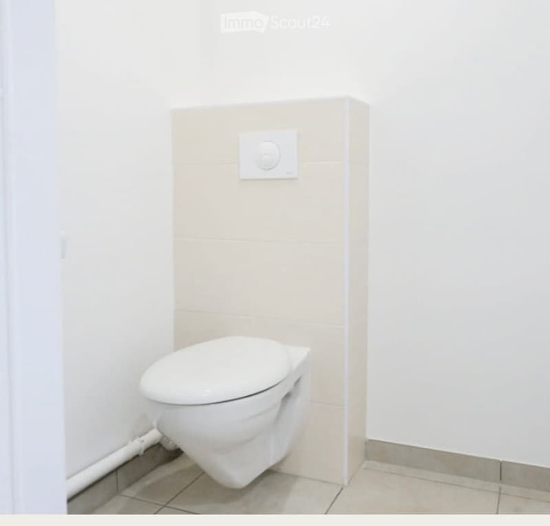 Modern bathroom with a white toilet, tiled floor, and a light switch on the wall.