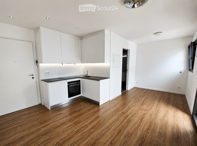 Modern, minimalist kitchen with white cabinets, black countertops, and a wooden floor. Features an oven, sink, and faucet.