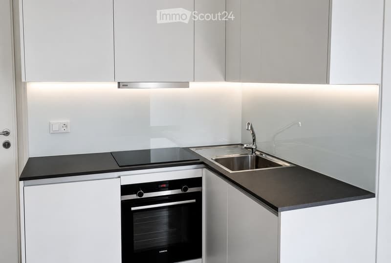 Modern kitchen with white cabinets, black countertops, a built-in oven, and a sink with a modern faucet.