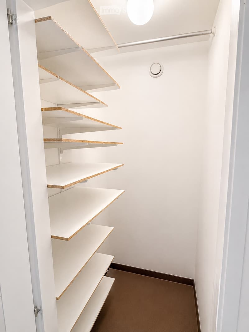 Modern, minimalist hallway with built-in white shelves featuring wooden trim, white walls, and a round ceiling light fixture.