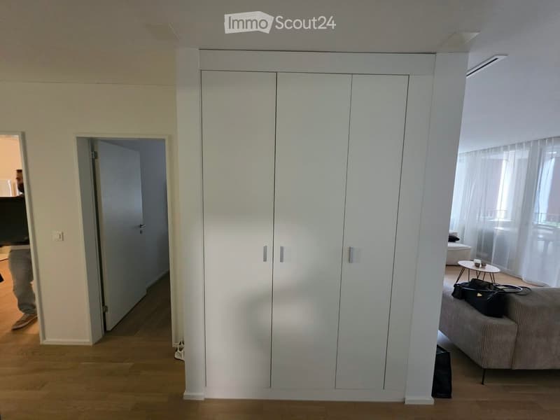 A modern hallway with a large white built-in wardrobe, a small round table with cups, and a sofa with a bag on it.