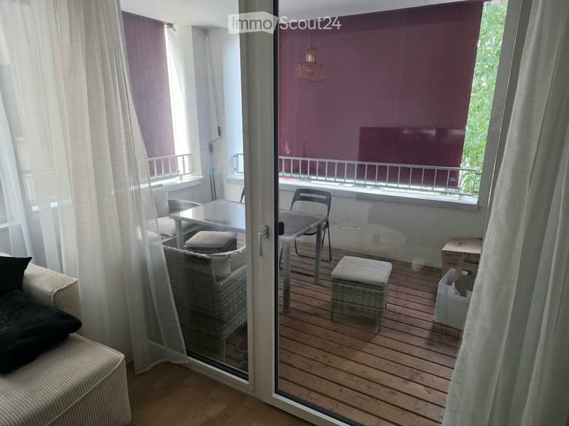 Balcony with wooden decking, glass sliding door, outdoor furniture including a table, chairs, and a sofa.