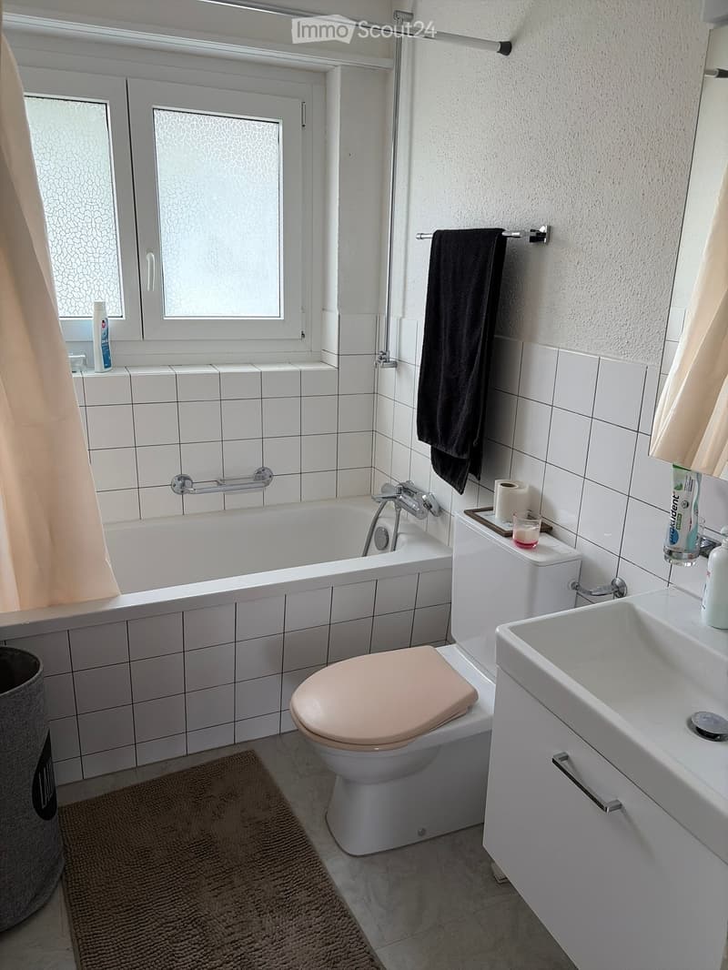Modern bathroom with white tiles, bathtub, toilet, sink, towel, and toiletries.