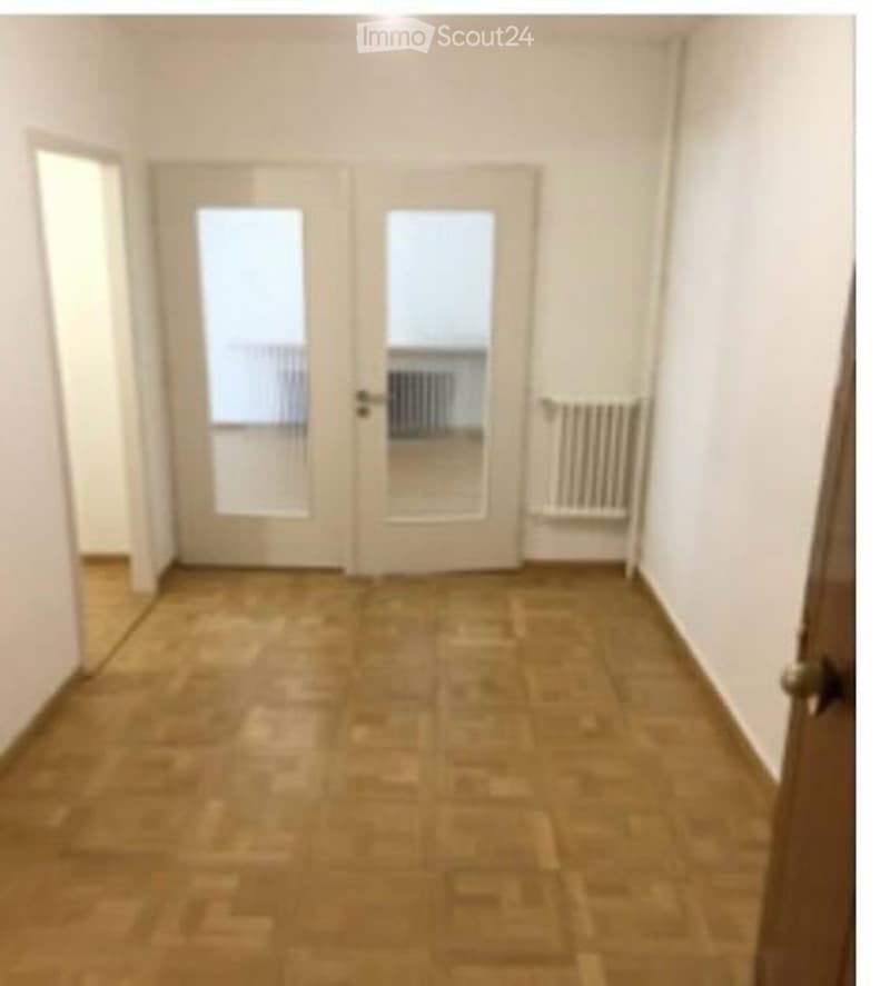 Empty room with wooden flooring, white walls, and a double door leading to another space. No furniture or equipment is present.