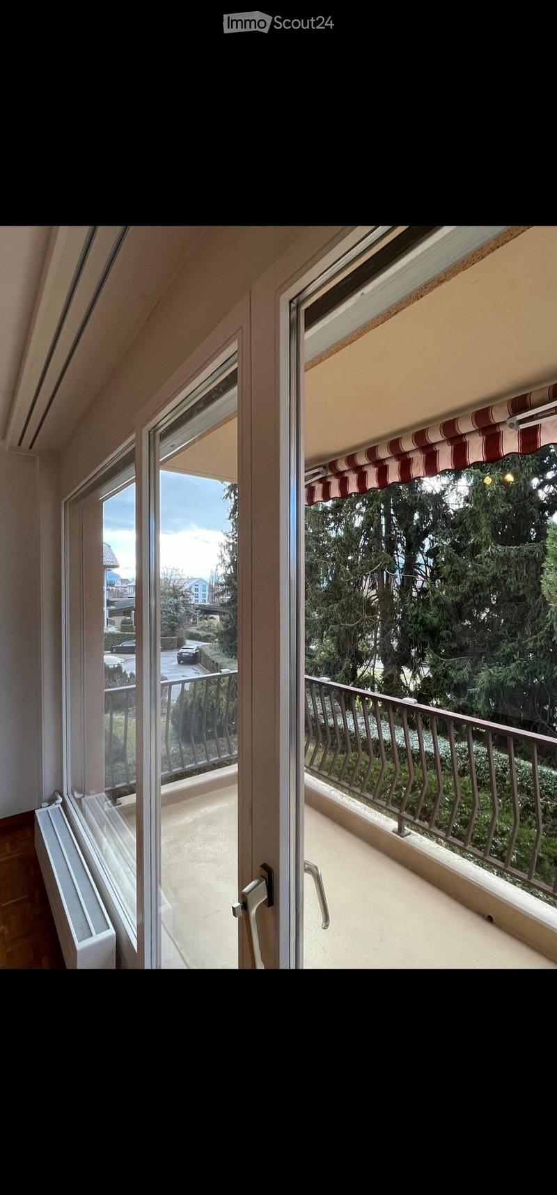 Balcony with metal railing, striped awning, and view of greenery and street.