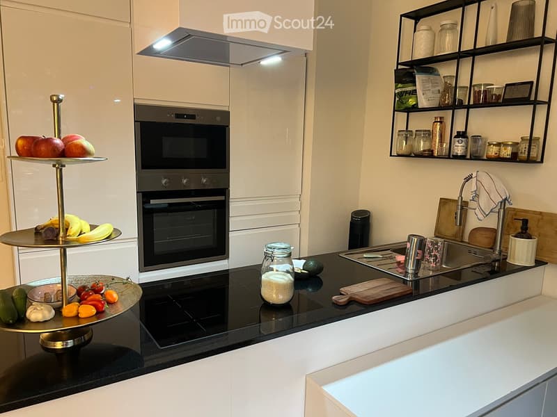 Modern kitchen with white cabinets, black countertops, stainless steel appliances, and a double-tiered fruit and vegetable display on the counter.