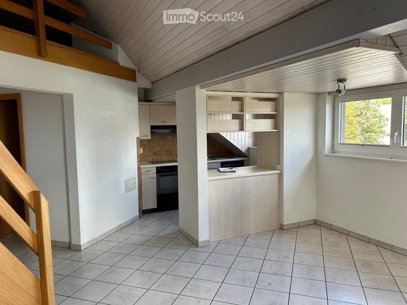 Bright kitchen with tiled floor, white walls, wooden counter, cabinets, and an oven. A staircase leads to an upper level.