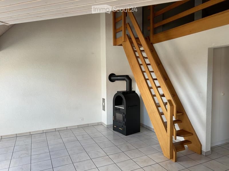 Hallway with wooden staircase leading to an upper level, featuring a black wood-burning stove with a chimney pipe.