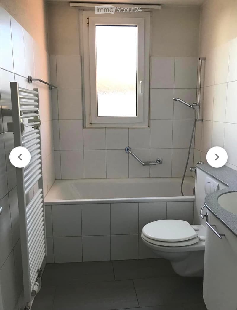 Modern bathroom with a bathtub, toilet, sink, radiator, and a window above the bathtub.