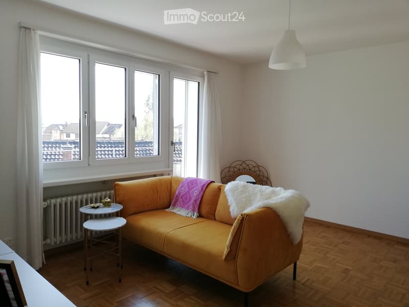 Living room with a mustard yellow sofa, two small tables, a mirror, and decorative throws.