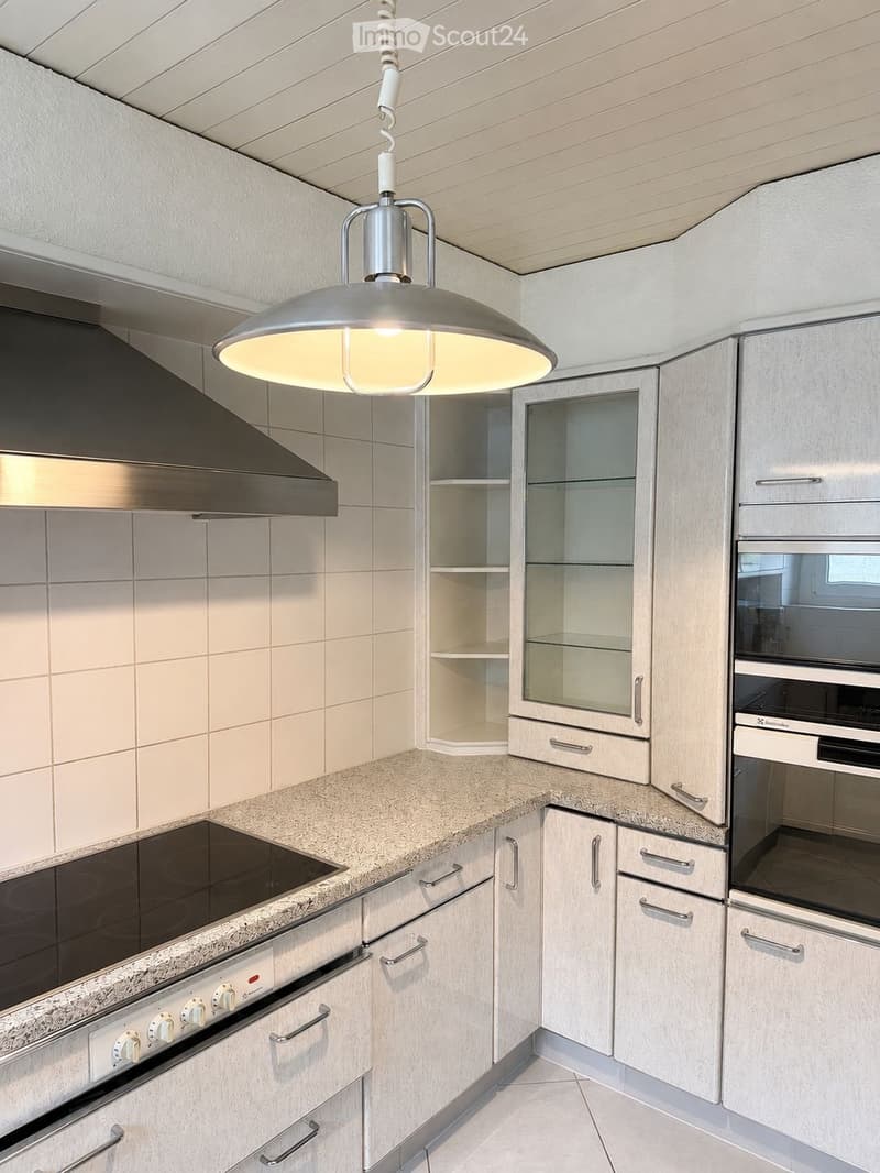Modern kitchen with light wood cabinets, granite countertops, stainless steel appliances, and a pendant light fixture.