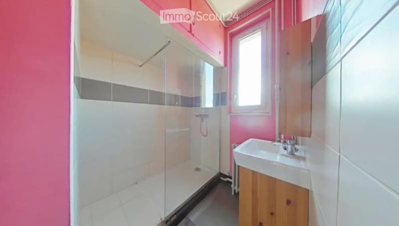 Modern bathroom with pink walls, white tiles, a glass-enclosed shower, a white sink with a wooden cabinet, and a window for natural light.