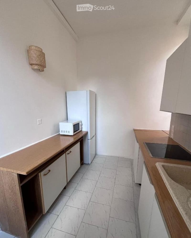 Modern kitchen with white tiled flooring, wooden countertops, white cabinets, a refrigerator, microwave, sink, and stove.