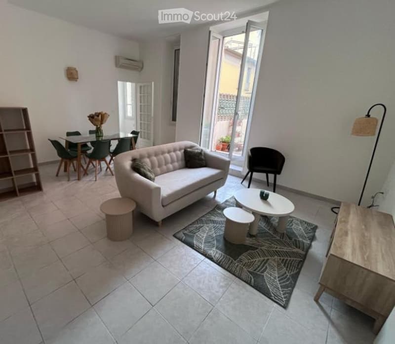 Bright living room with a white sofa, coffee table, dining area, and large windows opening to a balcony. Includes a floor lamp, side tables, and a shelf.