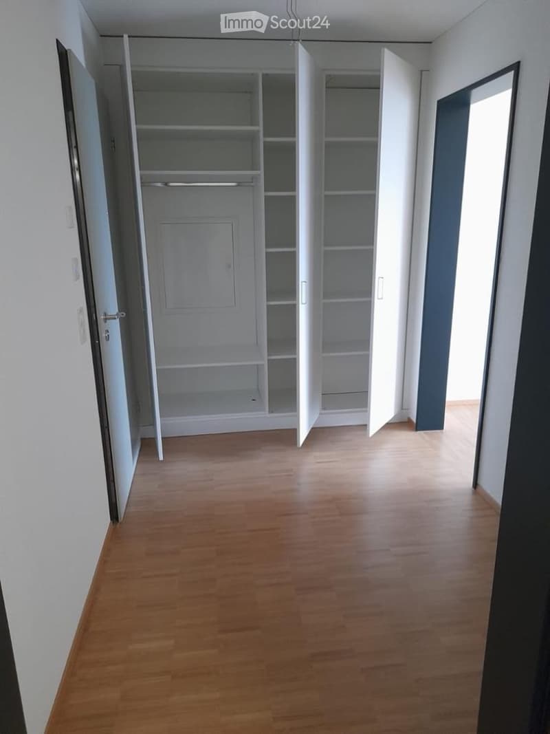 Empty room with wooden flooring, white walls, and an open closet with empty shelves and hanging space.