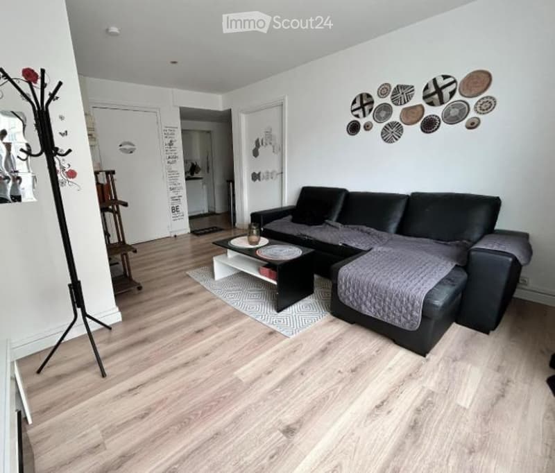 Modern living room with light wooden flooring, black sectional sofa, coffee table, decorative rug, and wall art featuring circular designs.