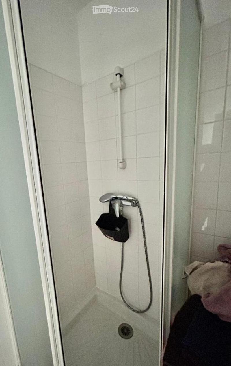 Shower area with white tiled walls, a fixed showerhead, handheld shower hose, and a drain in the floor.